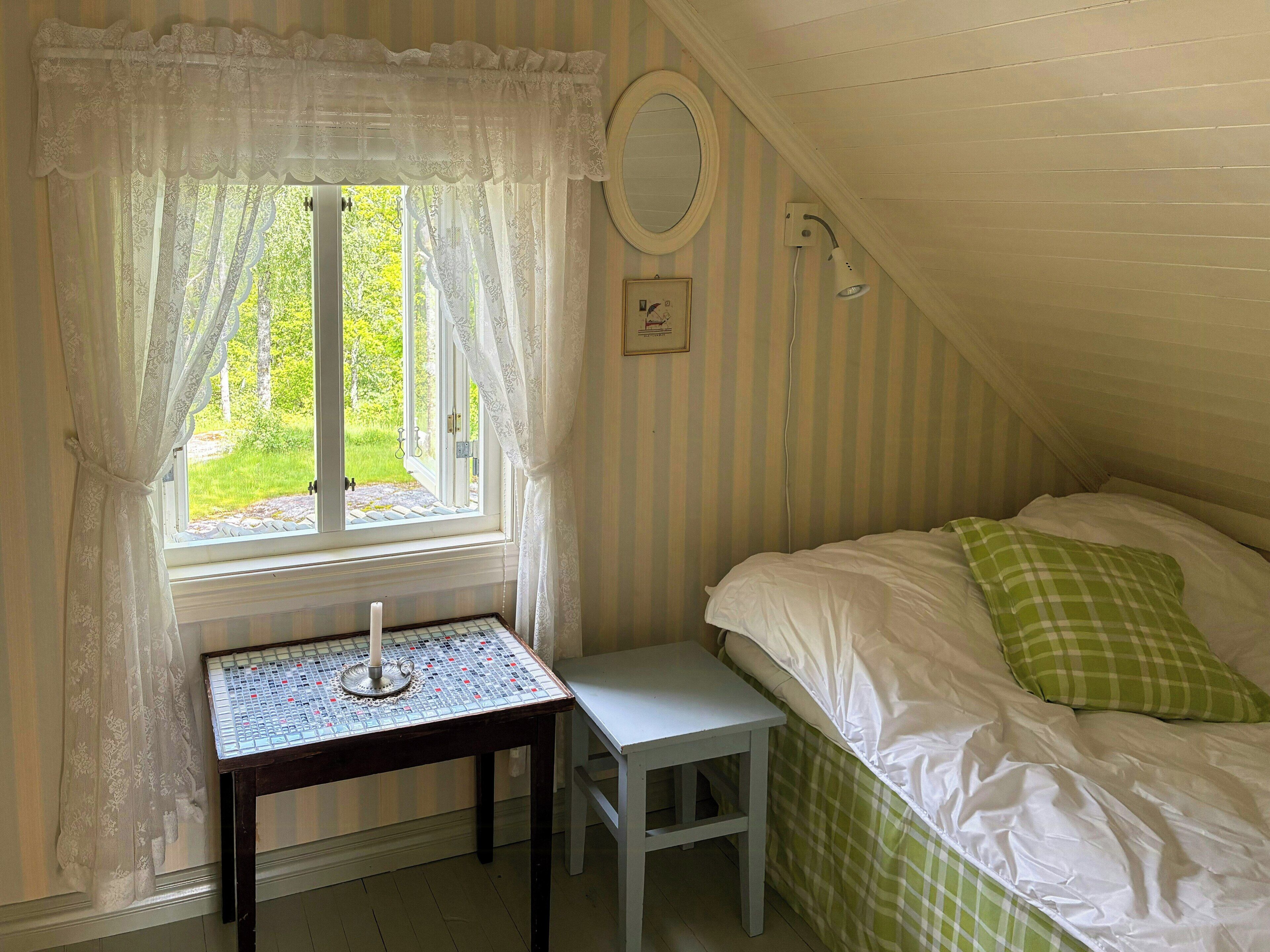 Un dormitorio con ventana, una mesita de noche, una lámpara, una cama con ropa de cama verde y blanca, y una pared a rayas.
