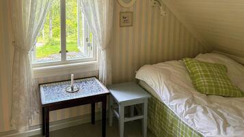 Un dormitorio con ventana, una mesita de noche, una lámpara, una cama con ropa de cama verde y blanca, y una pared a rayas.