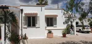 A two-story building with white walls and terracotta roof tiles, featuring two windows with shutters, potted plants, and a parked car. - Discover this elegant villa, with privat pool, nestled in Mediterrenean Salento (Lido Marini/Com. Salve)