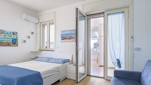 A bedroom with a bed, a chair, a sliding glass door, and a painting of boats on the wall. - Tamarè 3 by Casa di Marco (Conchiglie-Alto Lido)