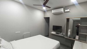 A hotel room with a bed, a desk, a chair, a ceiling fan, an air conditioning unit, a TV, and a mirror. - Sri Renga Inn (Tiruchirappalli)