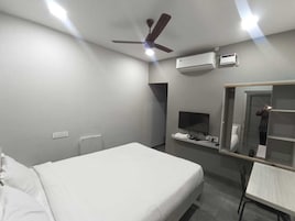 A hotel room with a bed, a desk, a chair, a ceiling fan, an air conditioning unit, a TV, and a mirror.