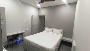 A bedroom with a bed, a desk, a chair, a ceiling fan, and a door. - Sri Renga Inn (Tiruchirappalli)