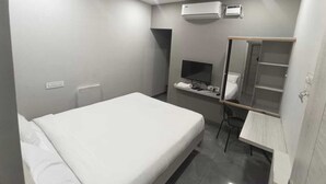 A bedroom with a bed, a desk, a chair, a TV, a mirror, an air conditioner, and a ceiling fan. - Sri Renga Inn (Tiruchirappalli)
