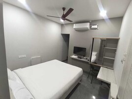 A bedroom with a bed, a desk, a chair, a TV, a mirror, an air conditioner, and a ceiling fan.