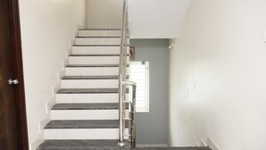 A staircase with a handrail, white walls, and a window with blinds. - Sri Renga Inn (Tiruchirappalli)