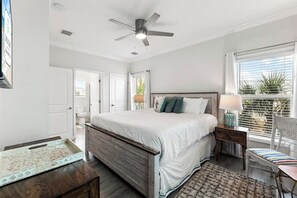 A bedroom with a bed, a ceiling fan, a window with blinds, and a view of a balcony.