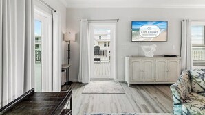 A modern living room with a TV, a view to the outside, a white cabinet, and a patterned sofa. - Mariner 1: BeachFront Cottage A, Gulf Front Views! (Mexico Beach)
