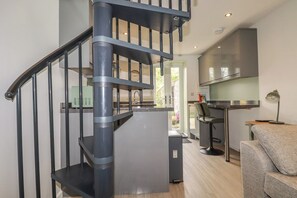 A modern kitchen with a built-in stove, a dining area with a table and chairs, and a spiral staircase with metal railings. - The Annex At The Barn (Liskeard)