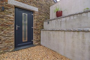 Pared exterior de piedra con una puerta, pared de hormigón con una planta en maceta y suelo de grava.