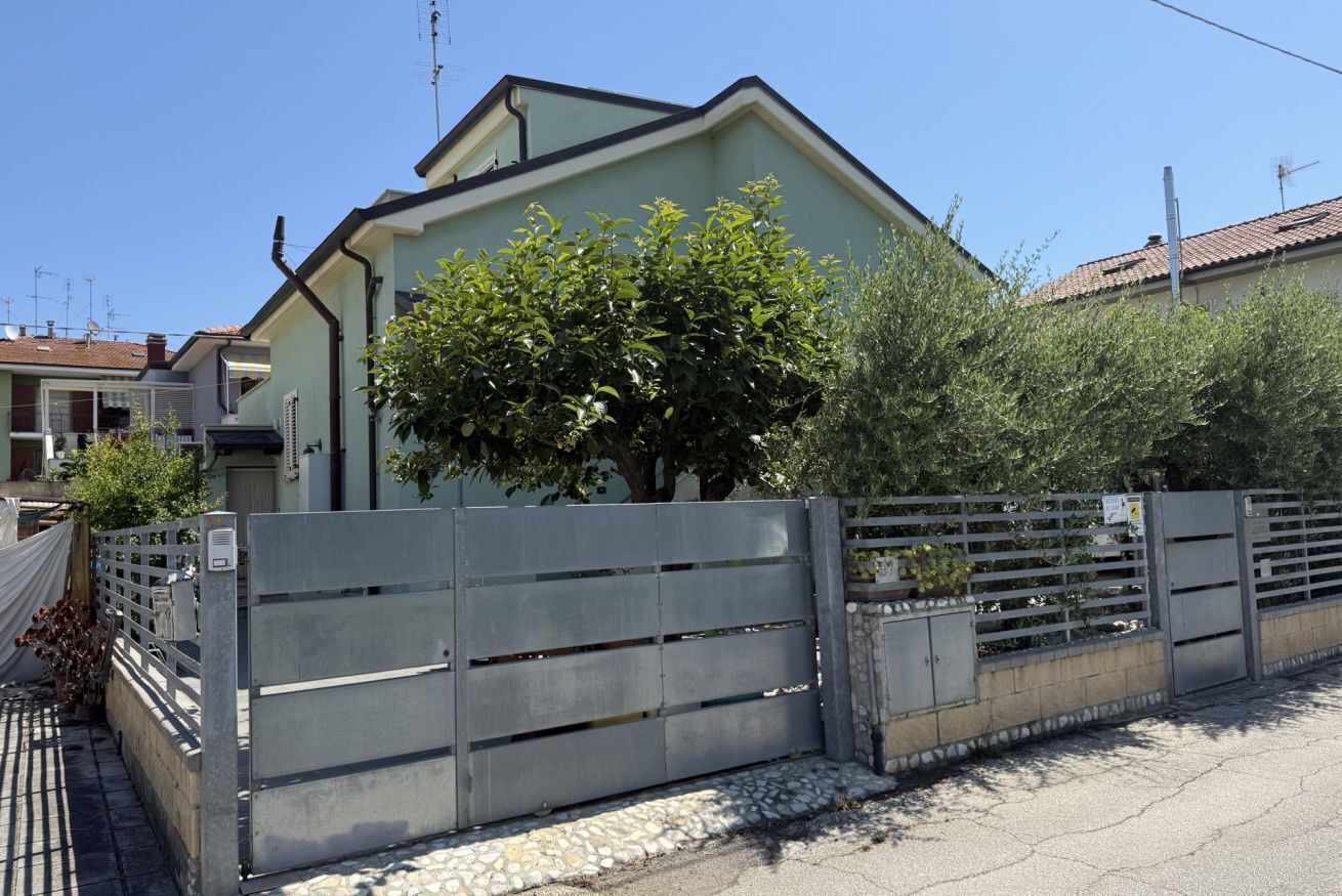 A residential building with a gated entrance, a tree in front, and a clear sky.