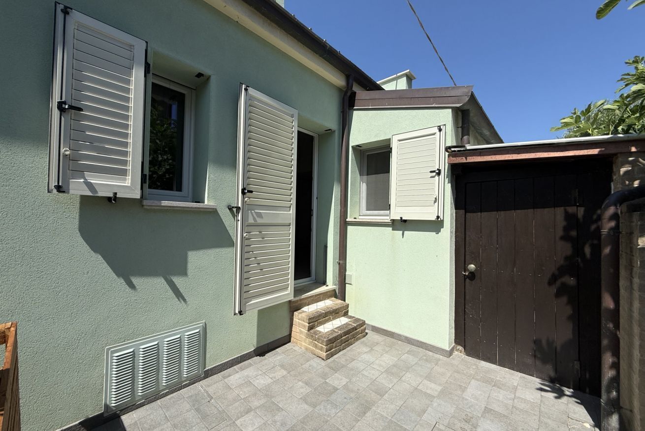 Ein Haus mit zwei offenen Fenstern, einer Tür und einer kleinen Treppe, die zum Eingang führt.