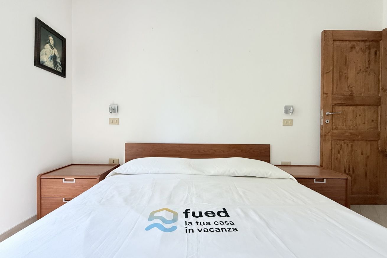Ein Schlafzimmer mit einem Bett, Nachttischen aus Holz, einem Kleiderschrank und einem gerahmten Bild an der Wand.