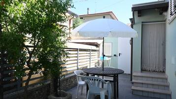 Un patio con una mesa y sillas, una sombrilla blanca y un muro de piedra.