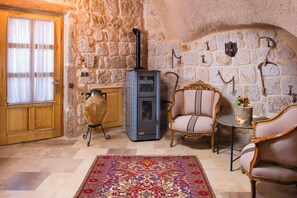 A room with a stone wall, a fireplace, a wooden door, and two upholstered chairs. - Dream Of Hotel (Nevşehir)