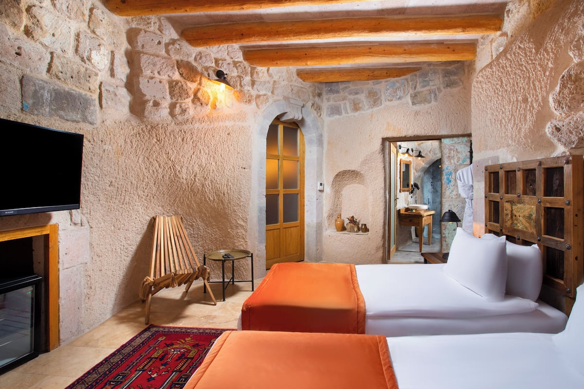 A rustic room with stone walls, a wooden ceiling, a bed, a TV, and a small table with a chair.