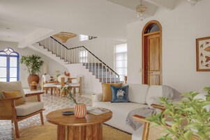 A spacious living area with a staircase, a dining set, and a sofa with decorative pillows.