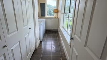 Um corredor com portas brancas, uma janela com vista para o verde e piso de azulejos.