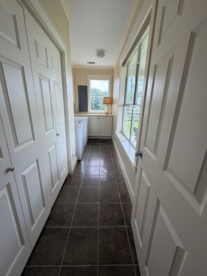 A hallway with white doors, a window with a view of greenery, and a tiled floor.