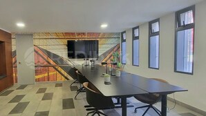 Kokoushuone, jossa on pitkä pöytä, tuoleja, televisioruutu ja värikäs seinämaalaus.