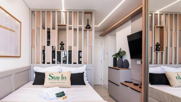A hotel room with a bed, a bedside table, a TV, a mirror, and a decorative wall panel.