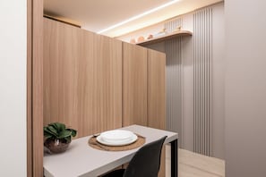 Un comedor con una mesa dispuesta para dos personas, una planta en maceta y una estantería con adornos.