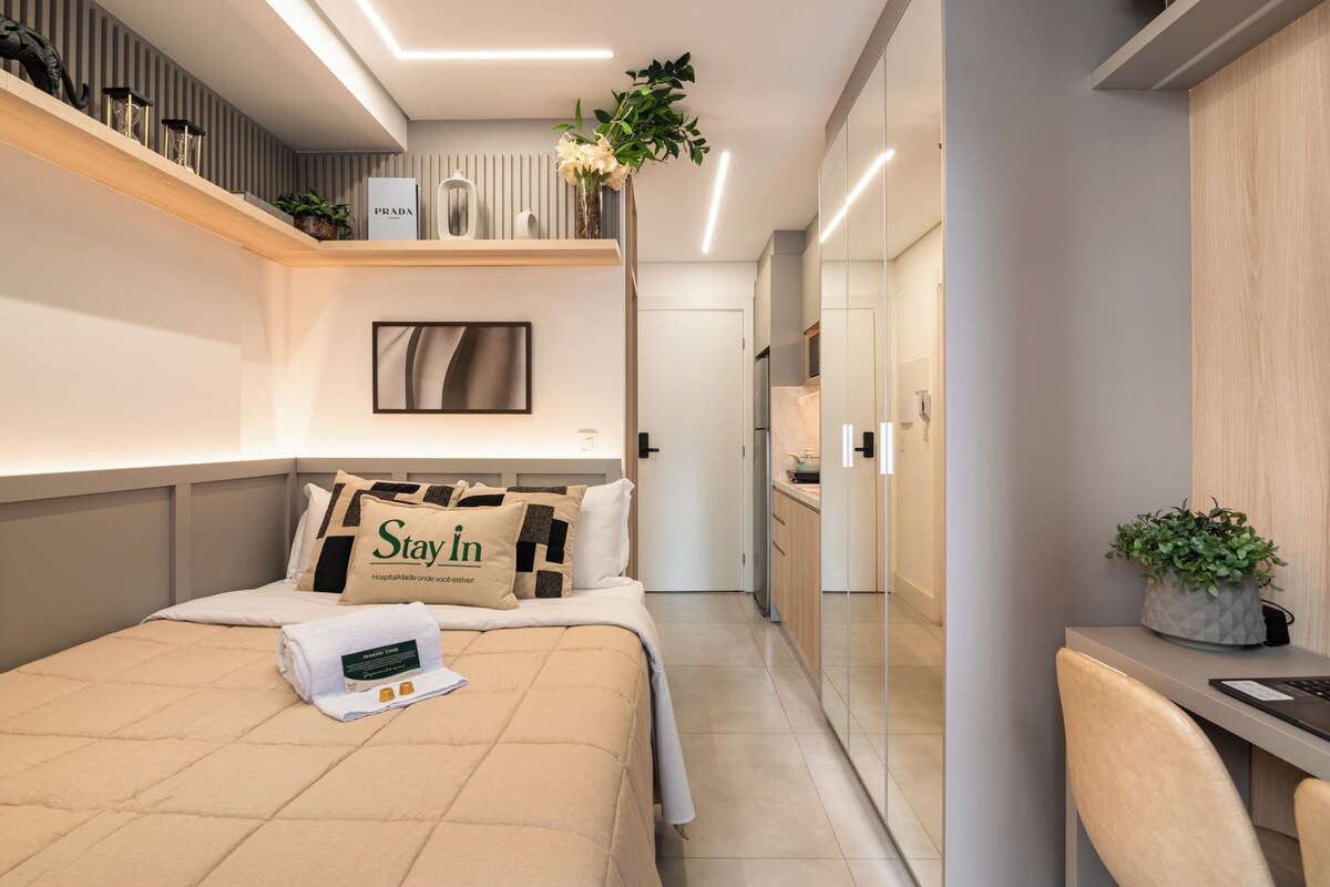 Una habitación de hotel moderna con una cama, un escritorio, un espejo y una planta.