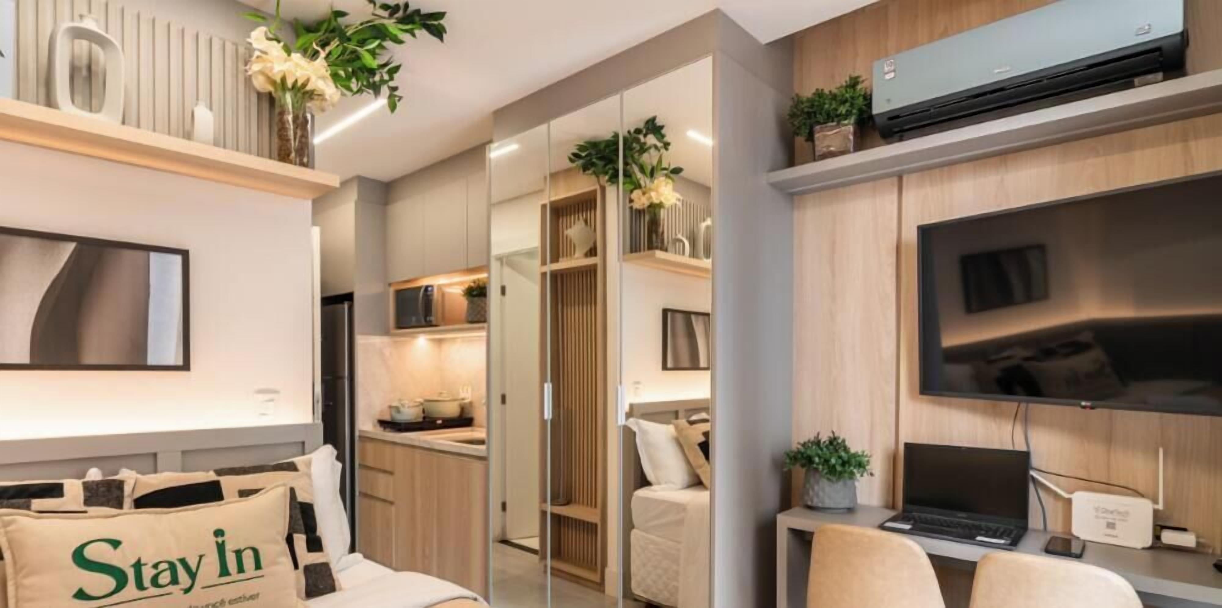 A modern hotel room with a bed, a desk with a laptop, a TV, and a minibar.