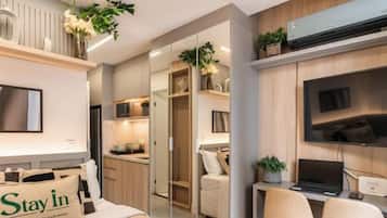 A modern hotel room with a bed, a desk with a laptop, a TV, and a minibar.