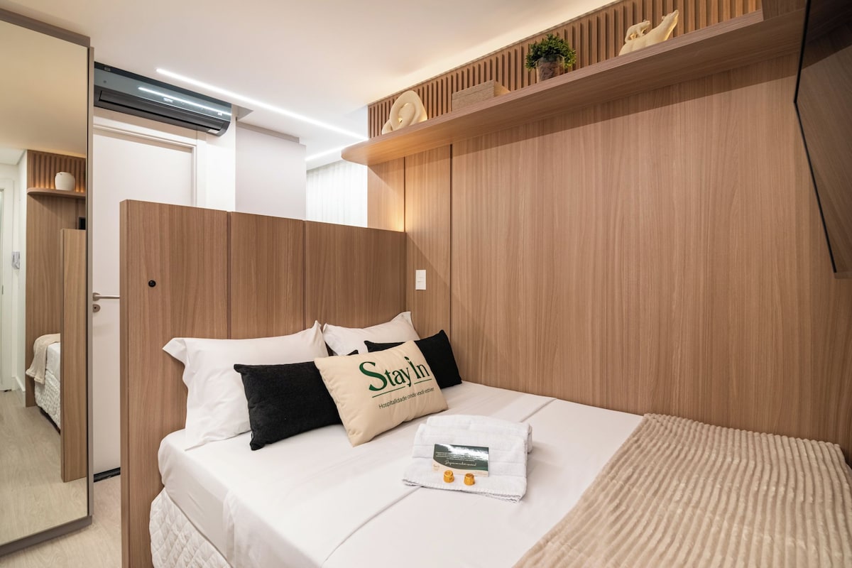 Una habitación de hotel con cama, mesita de noche, espejo y cabecero de madera.