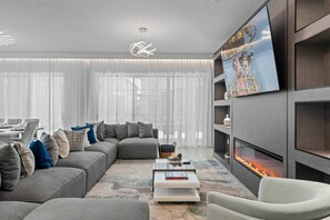 Ein modernes Wohnzimmer mit einem Ecksofa, einem Flachbildfernseher, einem Kamin und einem Essbereich im Hintergrund.