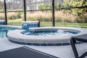 A hot tub area with a pool, surrounded by a glass enclosure and a view of a grassy landscape. - Spacious Luxury: 6BR Condo with Modern Amenities (Orlando)