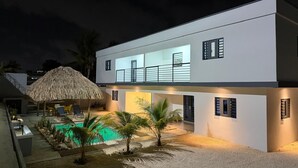 Una casa moderna de dos pisos con piscina, mobiliario exterior y una estructura de techo de paja.