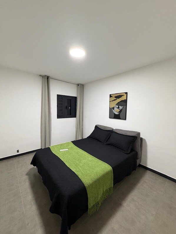 A bedroom with a bed, curtains, a painting, and a ceiling light.
