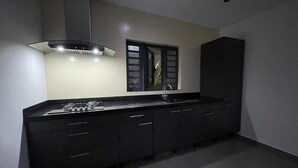 Una cocina moderna con encimera negra, lavamanos de acero inoxidable y campana extractora.