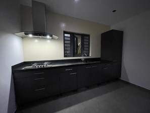 Una cuina moderna amb taulell negre, rentapeus d'acer inoxidable i campana extractora.