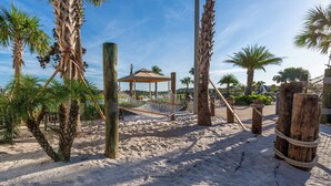 Een zandstrand met palmbomen, een hangmat en een houten constructie.