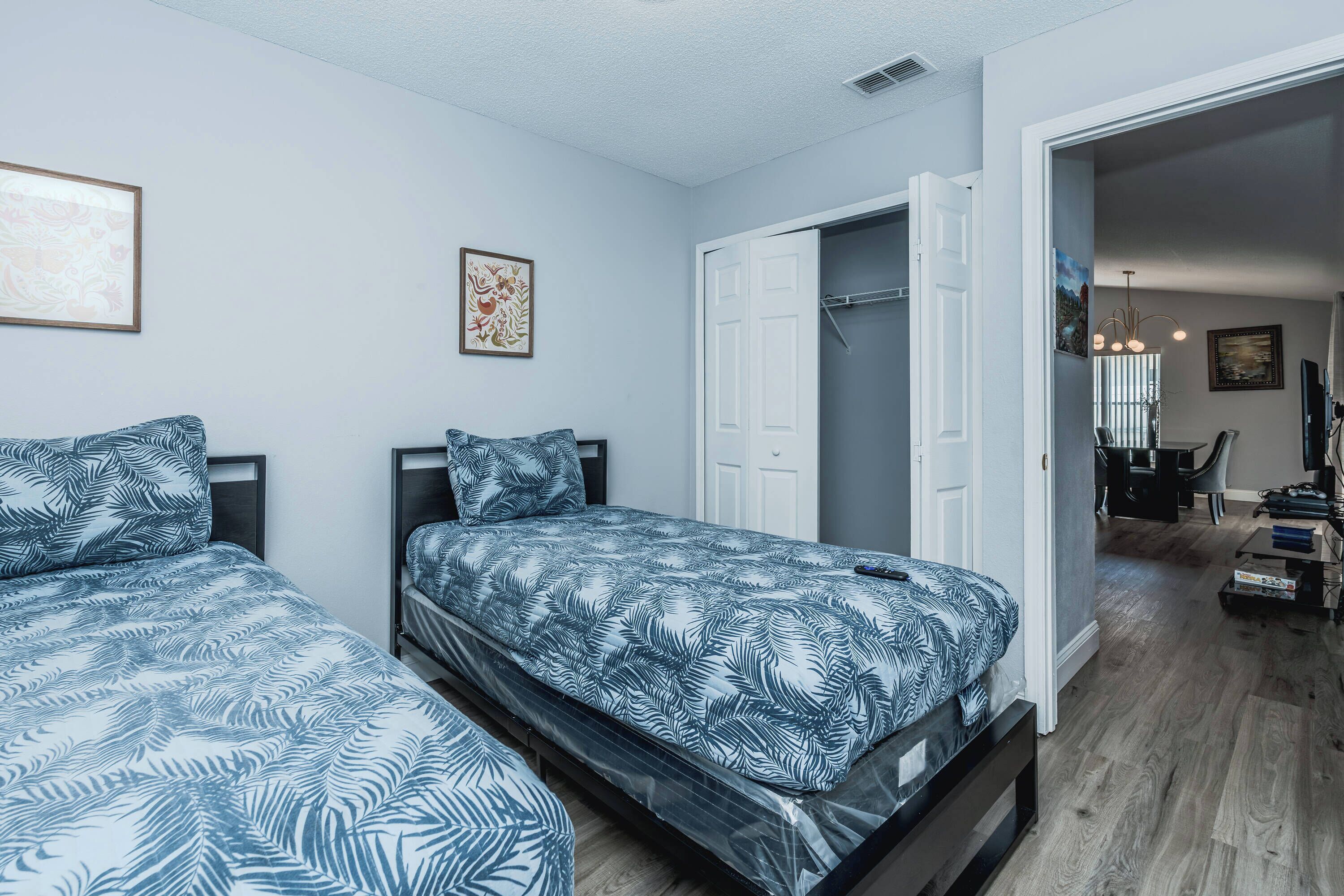 A bedroom with two beds, a wardrobe, and a door leading to a dining area.