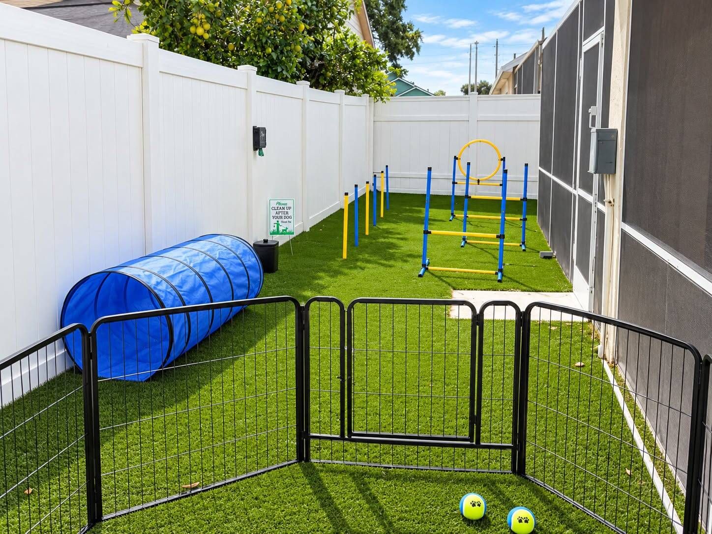 A fenced outdoor area with artificial grass, a blue tunnel, agility equipment, and a sign instructing to clean up after dogs.