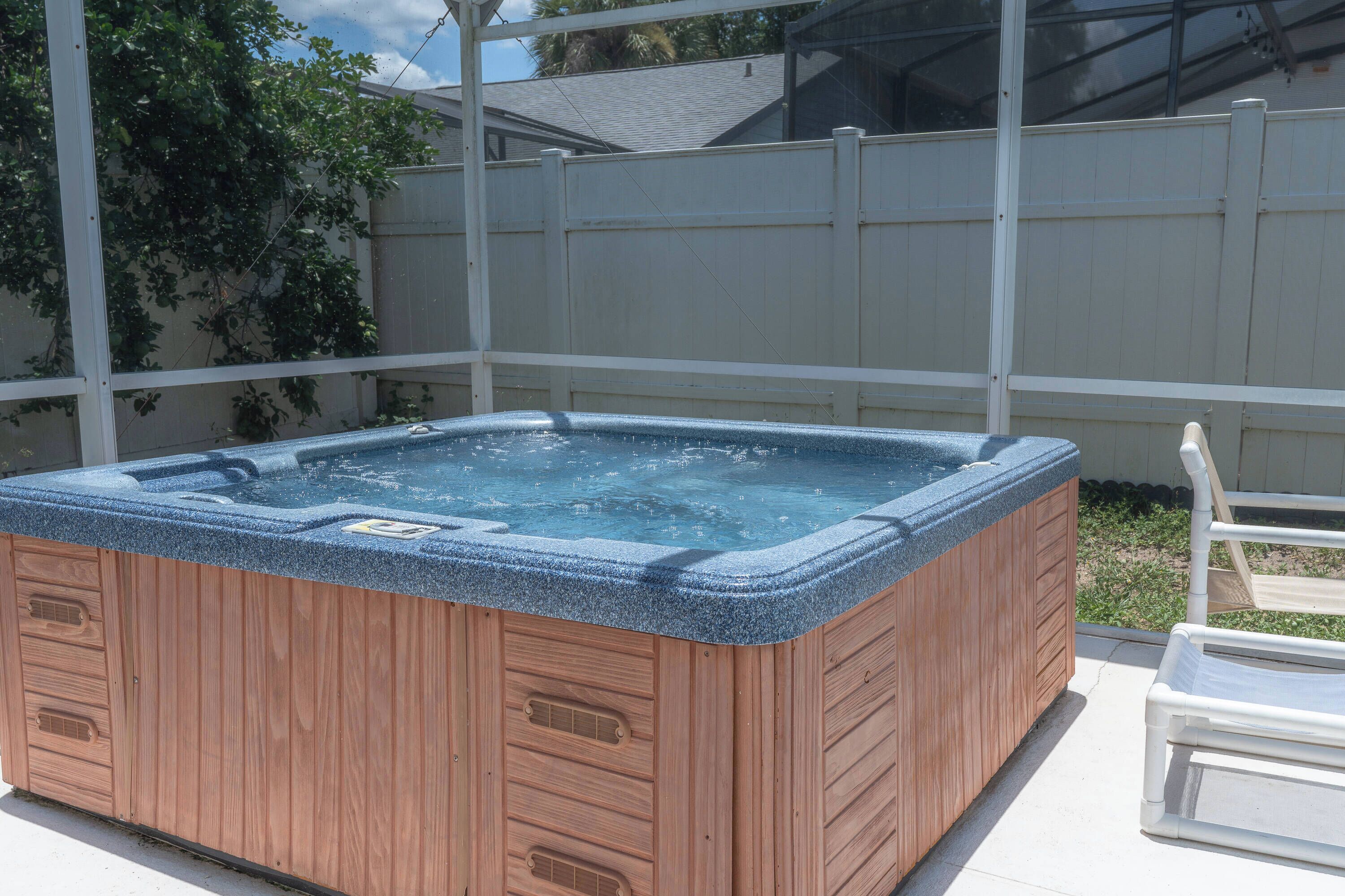 A wooden hot tub with a blue exterior, surrounded by a white fence and a clear sky.