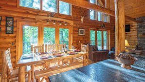 Ein Holzblockhaus-Innenraum mit Esstisch für vier Personen, Kamin und großen Fenstern.