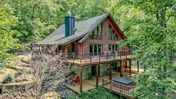 Eine zweistöckige Holzblockhütte mit einem Balkon, umgeben von Bäumen.