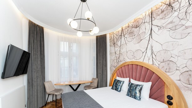 Quarto de hotel moderno com uma cama grande, uma escrivaninha e televisão fixada na parede.