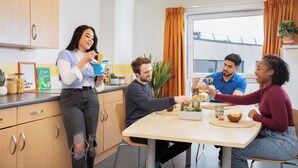 A group of people dining at a table in a modern kitchen with wooden cabinets and a window with curtains. - Unite - Harriet Martineau - Birmingham (Birmingham)