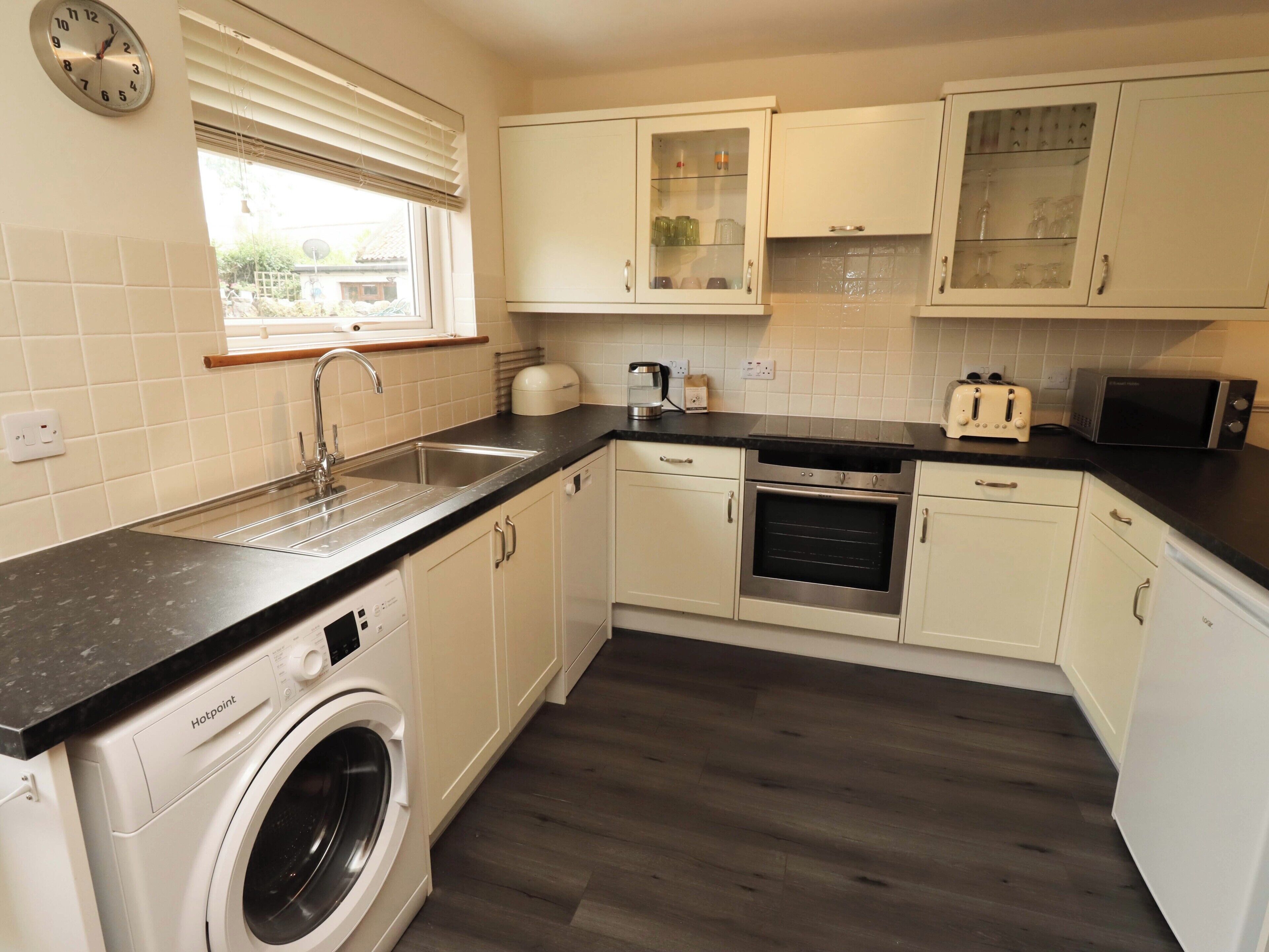 A kitchen with a washing machine, a sink, a toaster, an oven, and cabinets.