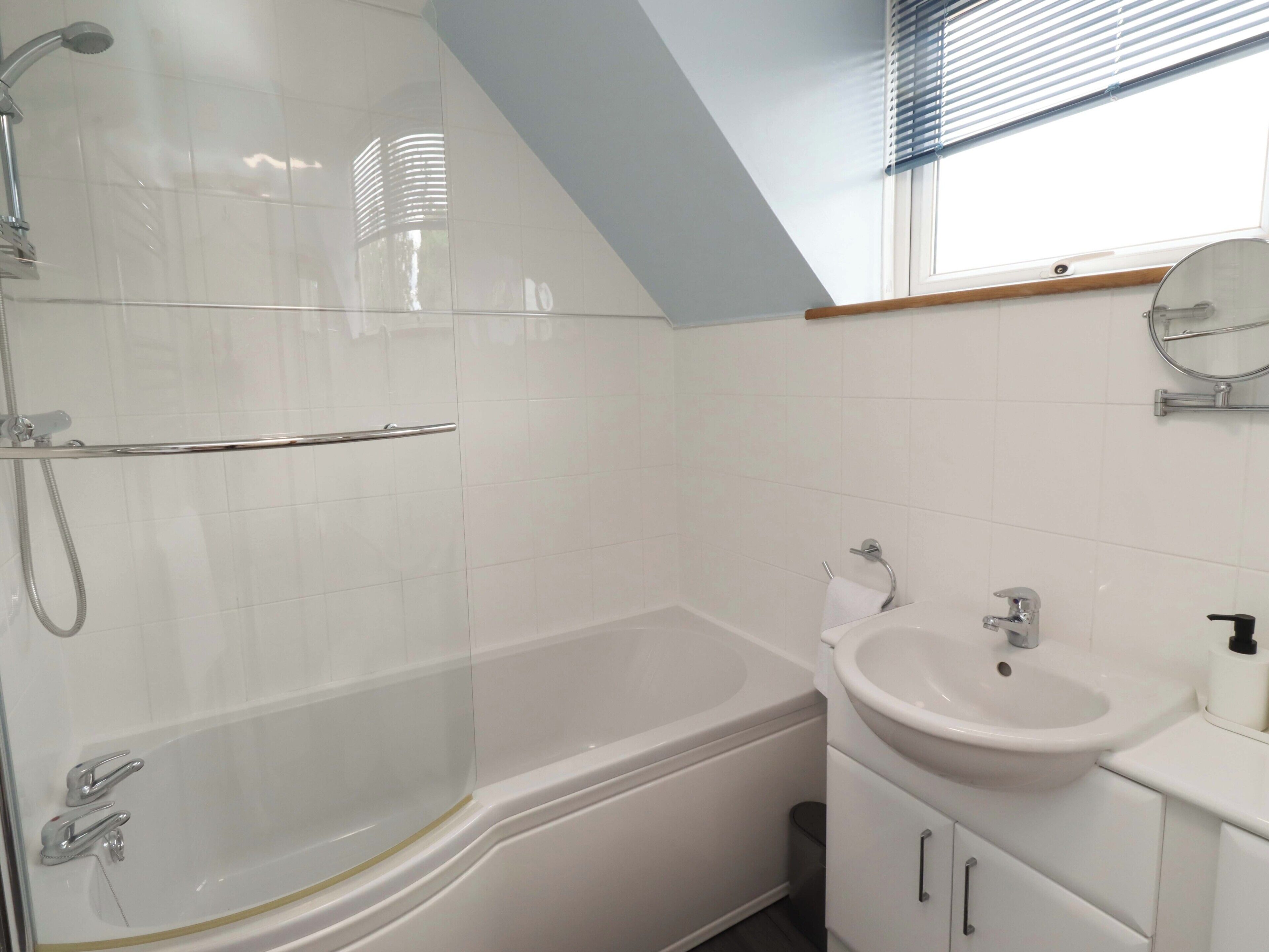 Un baño moderno con ducha de vidrio, bañera independiente, lavamanos con espejo y ventana con persianas.