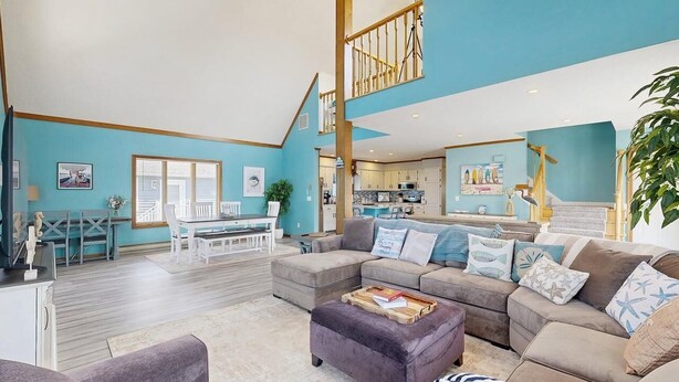 A spacious living area with a large sofa, a dining table, and a kitchen in the background. - Keen-Wik on the Bay - 38138 Keenwik Rd (Selbyville)