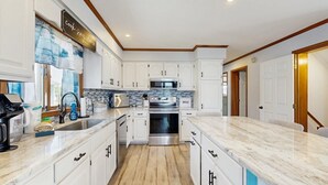 A modern kitchen with white cabinetry, a stainless steel oven, and a marble countertop. - Keen-Wik on the Bay - 38138 Keenwik Rd (Selbyville)