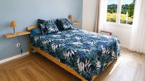 Un dormitorio con cama, cabecera de madera, lámparas de noche, ventana con vistas y toma de corriente.