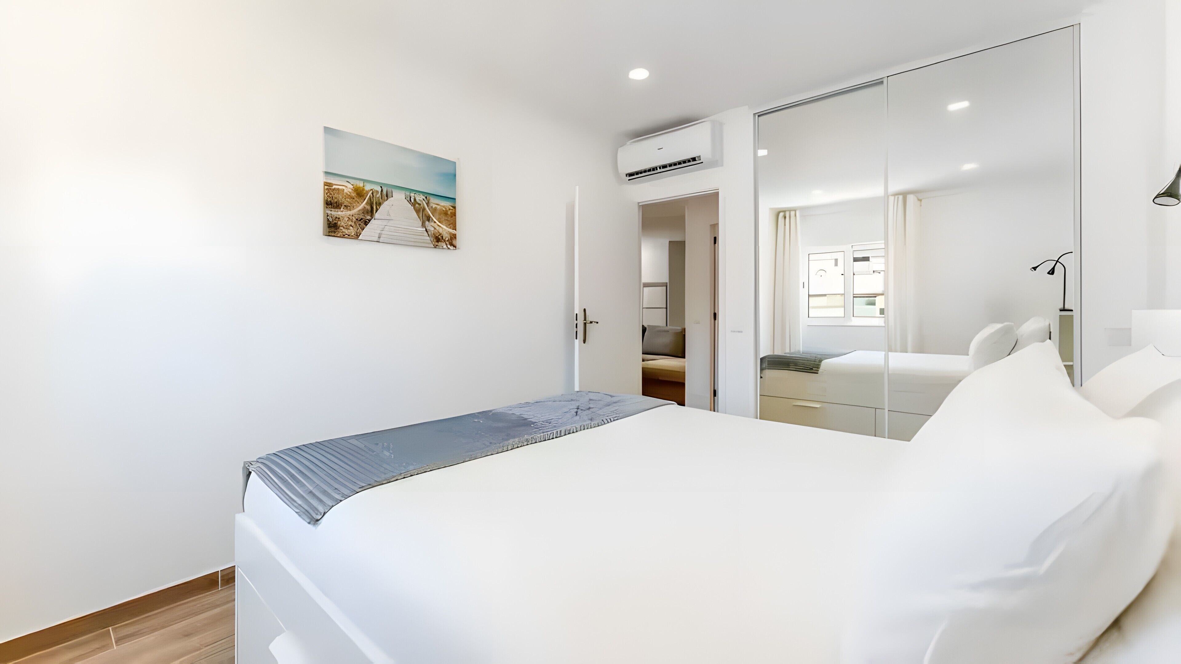 A modern bedroom with a bed, a painting, an air conditioning unit, and a mirror.